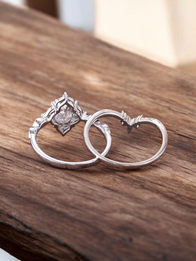 Puede incluir: Dos anillos de plata, uno con una gran piedra preciosa transparente engastada en un dise&ntilde;o decorativo e intrincado. Los anillos est&aacute;n sobre una superficie de madera.
