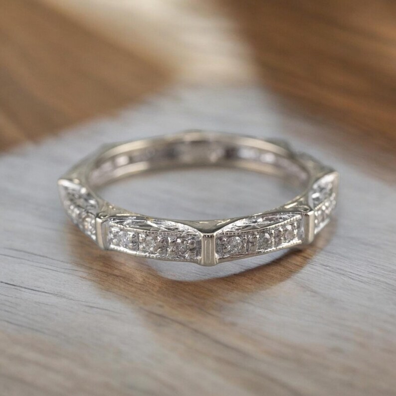 K&ouml;nnte beinhalten: Ein silberner Bandring mit einer Reihe kleiner Diamanten, die in einem dekorativen Design eingefasst sind.