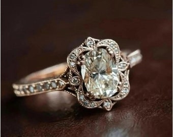 May include: A rose gold engagement ring with a large oval-shaped diamond surrounded by smaller diamonds. The ring has a delicate, vintage-inspired design.