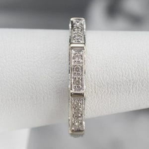 K&ouml;nnte beinhalten: Ein silberner Bandring mit einem filigranen, komplizierten Design, das mit kleinen Diamanten in Pav&eacute;-Fassung besetzt ist.