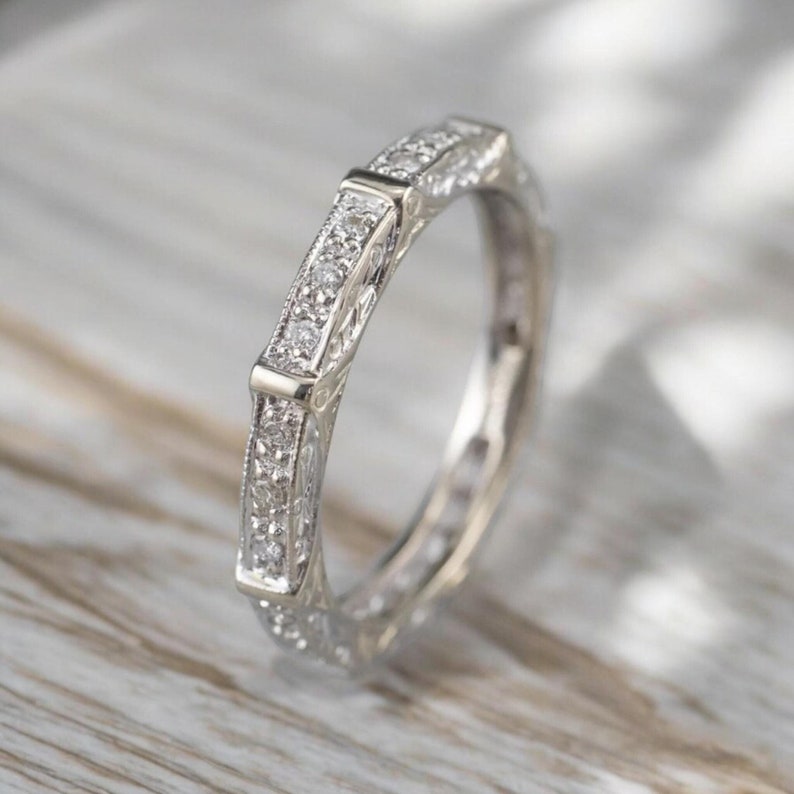 K&ouml;nnte beinhalten: Ein silberner Bandring mit einem filigranen, komplizierten Design, das mit kleinen Diamanten besetzt ist. Der Ring ist klassisch und elegant.