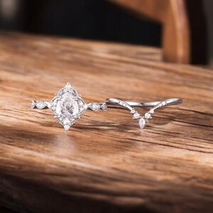 Puede incluir: Un anillo de compromiso de plata con una piedra central en forma de pera y una banda de boda contorneada a juego. El anillo est&aacute; engastado con peque&ntilde;as piedras redondas.