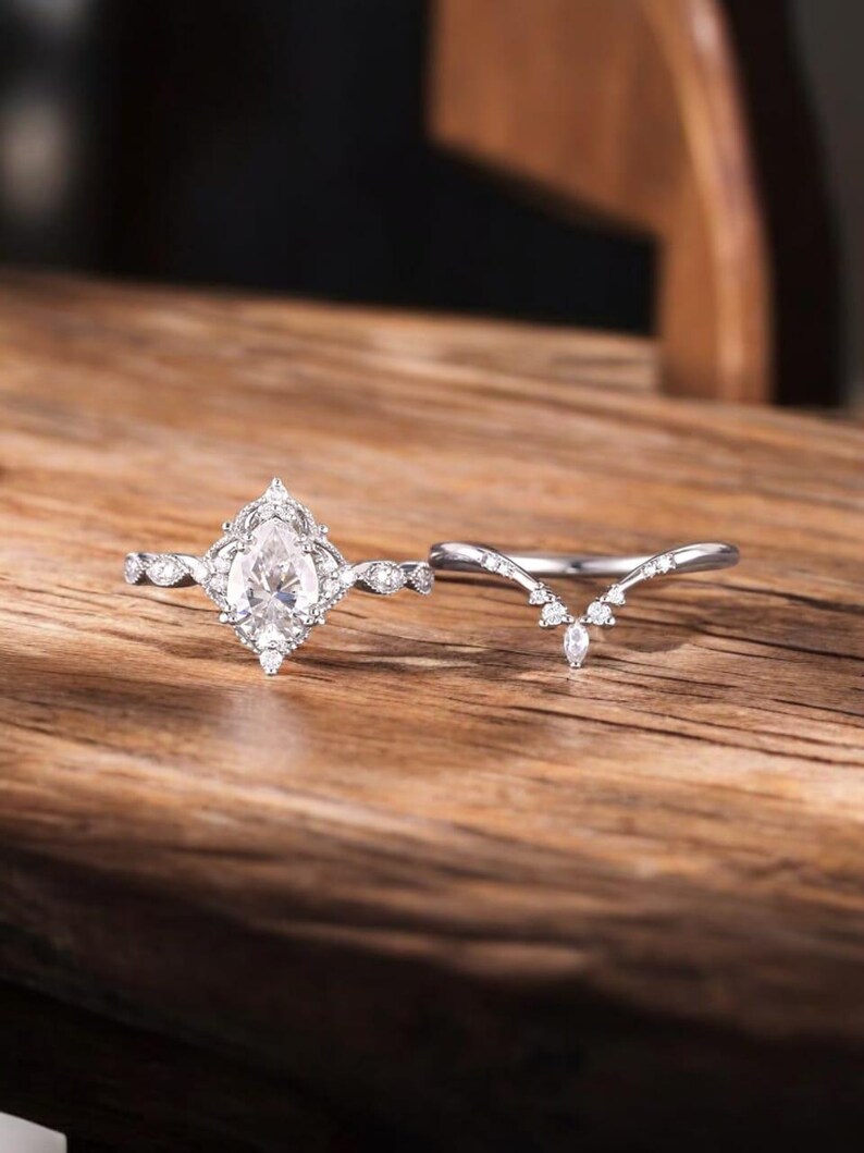 Puede incluir: Un anillo de compromiso de plata con una piedra central en forma de pera y una banda de boda contorneada a juego. El anillo est&aacute; engastado con peque&ntilde;as piedras redondas.