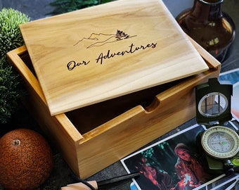 Może przedstawiać: Drewniana skrzynia z pokrywą, na której widnieje napis "Our Adventures". Skrzynia jest otwarta i zawiera zdjęcia, kompas i rozpałkę.