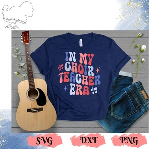 May include: A navy blue t-shirt with the text "In My Choir Teacher Era" in a retro font with musical notes and stars.