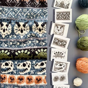May include: A knitted scarf with a detailed pattern featuring owls, pumpkins, and mountain designs in shades of green, blue, orange, and black. Accompanying the scarf are several pattern cards and balls of yarn.