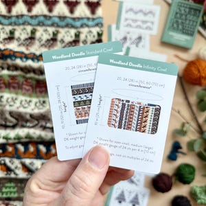 Peut inclure: Deux cartes "Woodland Doodle" sont tenues devant un col tricot&eacute;. Les cartes montrent des motifs et des mesures en pouces et en centim&egrave;tres. Le col pr&eacute;sente un motif r&eacute;p&eacute;t&eacute; de cerfs et de formes g&eacute;om&eacute;triques dans des tons de marron, de sarcelle et d'orange.