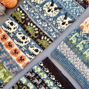May include: Close-up of several knitted items in shades of blue, green, orange, and black. The items feature repeating patterns of skulls and other geometric shapes. Several balls of yarn in orange, green, and gray are in the upper left corner.