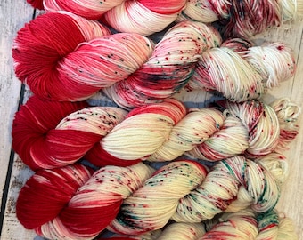 May include: Five skeins of yarn in a red and white colorway with green and black speckles. The yarn is twisted into a rope shape.