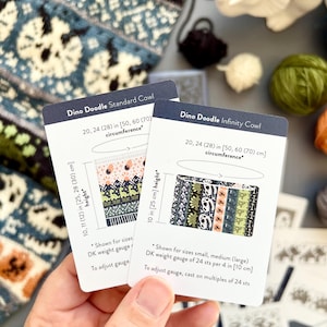 May include: Two cards with "Dino Doodle" cowl patterns are held in a hand. The "Standard Cowl" card shows a colorful design, while the "Infinity Cowl" card displays a pattern with dinosaurs. The cards include measurements in inches and centimeters.