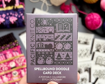 May include: A purple card deck labelled "Spellbound Doodle Card Deck" featuring spooky illustrations. The text reads "A portable colorwork stitch dictionary." The card is held in a hand, with knitting supplies and a skull in the background.