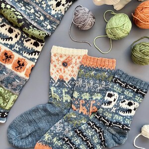 May include: A collection of hand-knitted socks in shades of blue, orange, green, and cream, featuring intricate patterns and designs. The image also includes balls of yarn in various colors and a white ceramic dinosaur figurine, suggesting a craft or hobby theme.