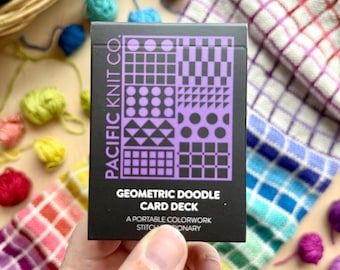 May include: A black rectangular card deck box with purple geometric patterns and the text Pacific Knit Co. Geometric Doodle Card Deck A Portable Colorwork Stitch Dictionary printed in white and purple on the front surface of the packaging.
