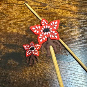 以下が含まれることがあります： 2つのデモゴルゴンをテーマにしたケーキトッパー。トッパーは、白いアクセントが付いた赤い花のような頭と茶色の体を持っています。ケーキやカップケーキを飾るのに最適な木製の串に付いています。