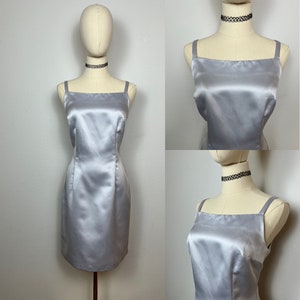 May include: A silver satin sleeveless dress with a square neckline. The dress is fitted and has a straight skirt.