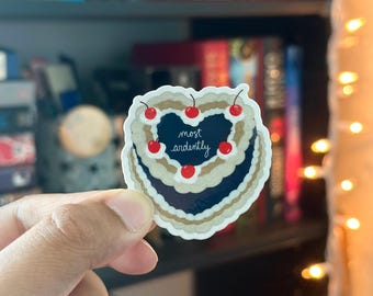 May include: A sticker of a heart-shaped cake with a black background and white frosting. The cake is decorated with red cherries and the text "most ardently" is written in white on the cake.