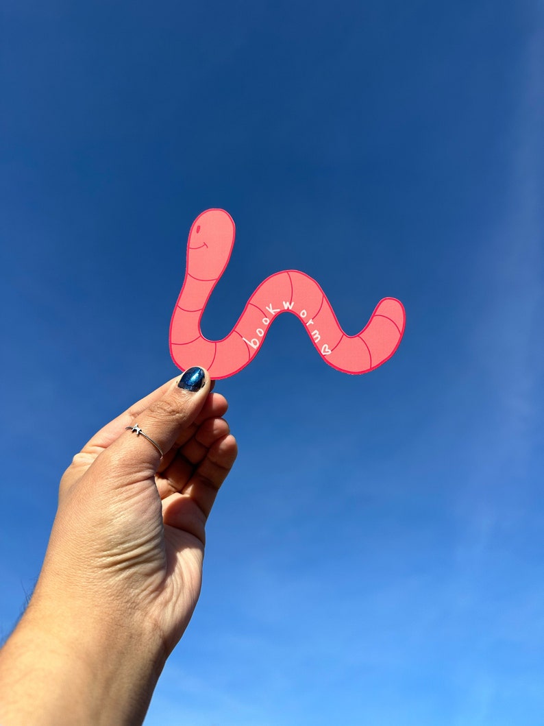 a pink bookmark in the shape of a wavy worm. Has darker pink stripes and a smile. Along the curve in the middle wave of the worm is the word "bookworm" written in white