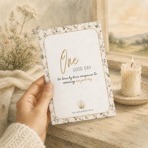 May include: A rectangular card with a floral border and gold-toned text that reads One GOOD DAY An hour-by-hour companion to receiving one good day and THE SMOLDERING WICK. The card features a central gold-toned circular icon and a white background.
