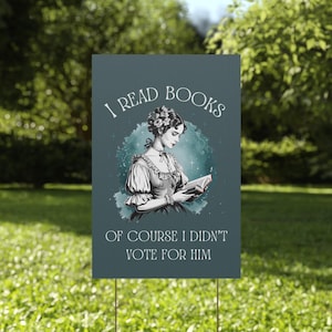 A green plastic yard sign featuring a watercolor image of a Victorian era woman reading a book and the words I READ BOOKS OF COURSE I DIDNT VOTE FOR HIM in white vintage lettering