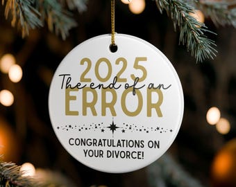 Puede incluir: Adorno navideño redondo de cerámica blanca con texto dorado. El texto dice "2025 The end of an ERROR" y "CONGRATULATIONS ON YOUR DIVORCE!". El adorno cuelga de un cordón dorado.