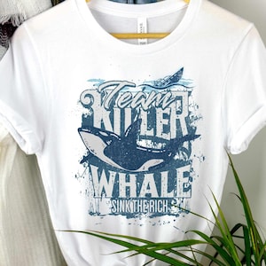 May include: White t-shirt with a blue and white graphic of a killer whale with the text "Team Killer Whale Sink The Rich" on it.