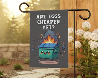 May include: A gray garden flag with a cartoon illustration of a green dumpster on fire. The text on the flag reads "Are eggs cheaper yet?"