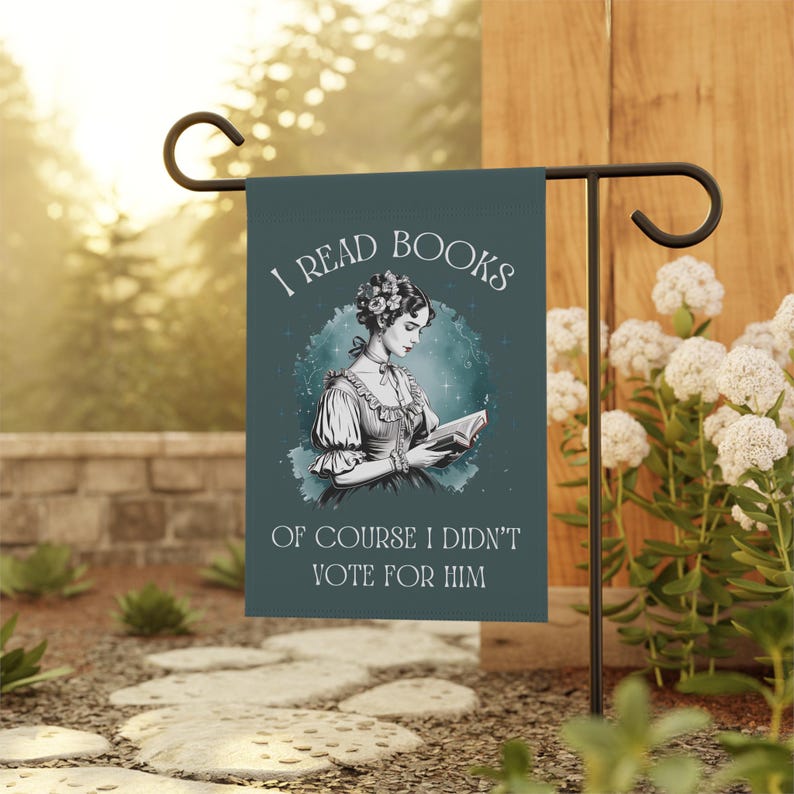 A green garden flag featuring a vintage illustration of a woman reading a book and the words I READ BOOKS OF COURSE I DIDNT VOTE FOR HIM in white vintage lettering