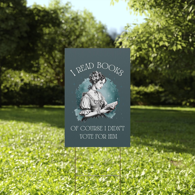 A green plastic yard sign featuring a watercolor image of a Victorian era woman reading a book and the words I READ BOOKS OF COURSE I DIDNT VOTE FOR HIM in white vintage lettering