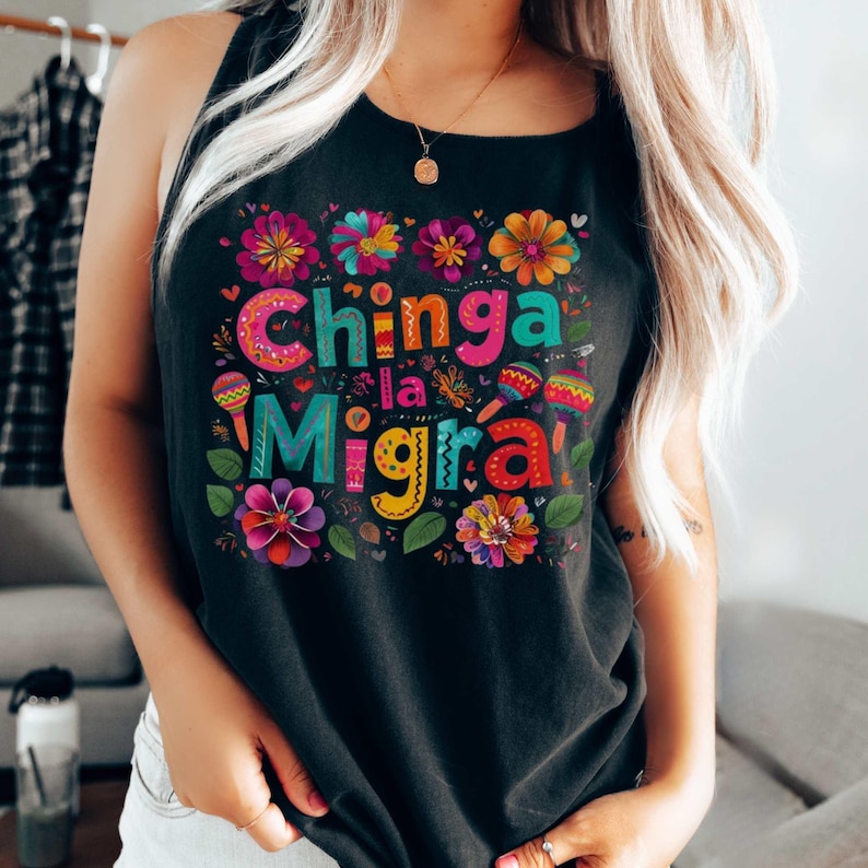 A woman wears a black tank top featuring a festive Mexican design with flowers and maracas surrounding the words CHINGA LA MIGRA