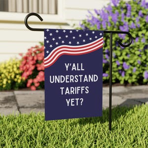 May include: A blue garden flag with a red, white, and blue American flag design. The text on the flag reads "Y'all understand tariffs yet?"