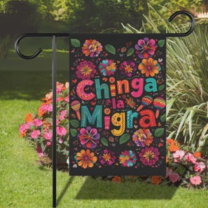 May include: A black garden flag with colorful floral designs and the text "Chinga la Migra" in vibrant letters. The flag is adorned with various flowers in shades of pink, orange, and purple, and is displayed on a black metal stand.