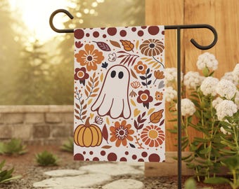 May include: A garden flag featuring a whimsical design for the fall season. The flag showcases a friendly ghost, pumpkins, and various floral elements in shades of orange, brown, and cream. The flag is displayed on a black metal stand, perfect for outdoor decor.