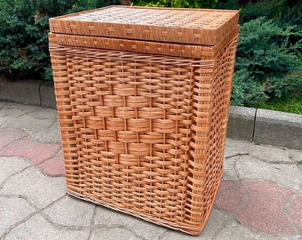 May include: A large, rectangular wicker basket with a lid. The basket is made of natural woven wicker and has a light brown color.