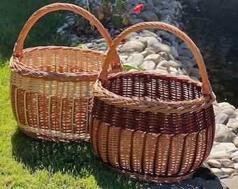 May include: Two woven wicker baskets with handles. The baskets are brown and white with a natural wood finish. The baskets are sitting on a bed of green grass.