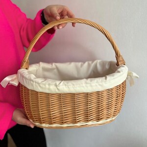 Peut inclure: Un panier en osier tress&eacute; avec une doublure en tissu blanc et une poign&eacute;e en ruban blanc. Le panier est de forme ovale et de couleur brun naturel.