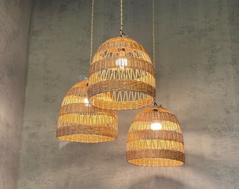 May include: Three woven wicker pendant lights hang from the ceiling. The lights are a light brown colour and have a natural, rustic look.