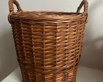 May include: A brown wicker basket with two handles. The basket is woven with a tight pattern and has a rounded bottom.