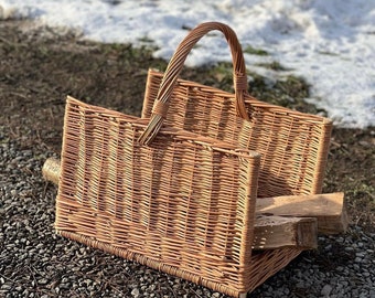 May include: A woven wicker log basket with a handle. The basket is filled with a few pieces of firewood. The basket is sitting on a gravel surface.