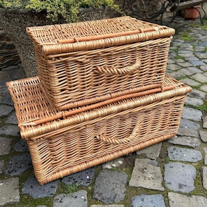 May include: Two woven wicker baskets stacked on top of each other. The top basket has a lid and the bottom basket is open. Both baskets have handles.