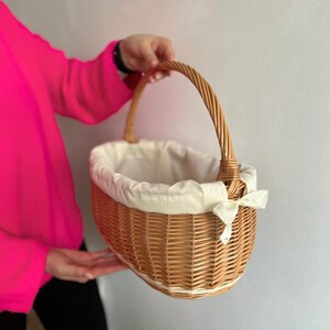 Peut inclure: Un panier en osier tress&eacute; avec une doublure en tissu blanc et un ruban blanc. Le panier a une poign&eacute;e et est de forme ovale.