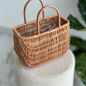 May include: A woven wicker basket with two handles. The basket is light brown and has a rectangular shape.