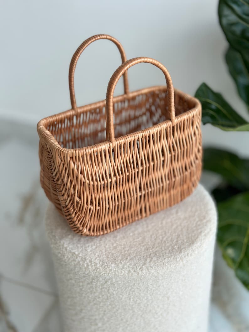 May include: A woven wicker basket with two handles. The basket is light brown and has a rectangular shape.