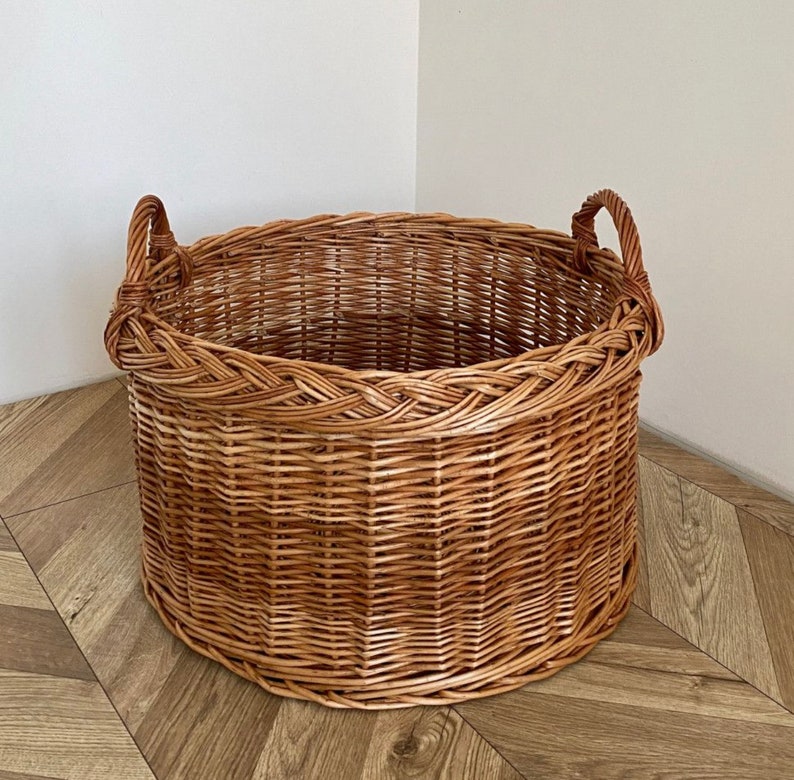 May include: A large, round wicker basket with two handles. The basket is made of natural woven wicker and has a light brown color.