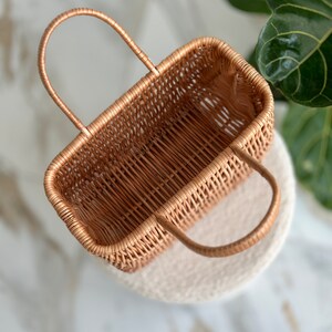 May include: A woven wicker basket with two handles. The basket is empty and has a light brown color.