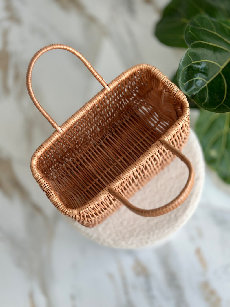 May include: A woven wicker basket with two handles. The basket is empty and has a light brown color.