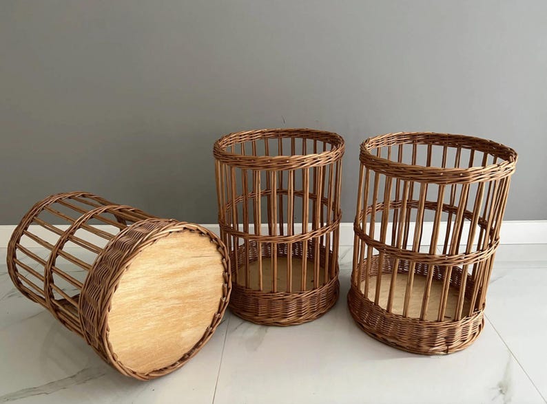Puede incluir: Tres cestas cil&iacute;ndricas hechas de mimbre trenzado marr&oacute;n. Cada cesta presenta un dise&ntilde;o de listones verticales con una base circular de madera maciza de color claro. Dos cestas est&aacute;n de pie, mientras que una est&aacute; de lado, revelando la base.