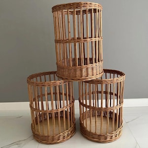 May include: Three cylindrical wicker baskets. The baskets are made of woven brown wicker and have a vertical slat design. The baskets are different sizes and are arranged in a group. The baskets have a natural, rustic appearance.