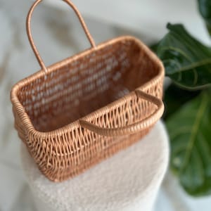 May include: A woven wicker basket with a single handle. The basket is light brown and has a rectangular shape.