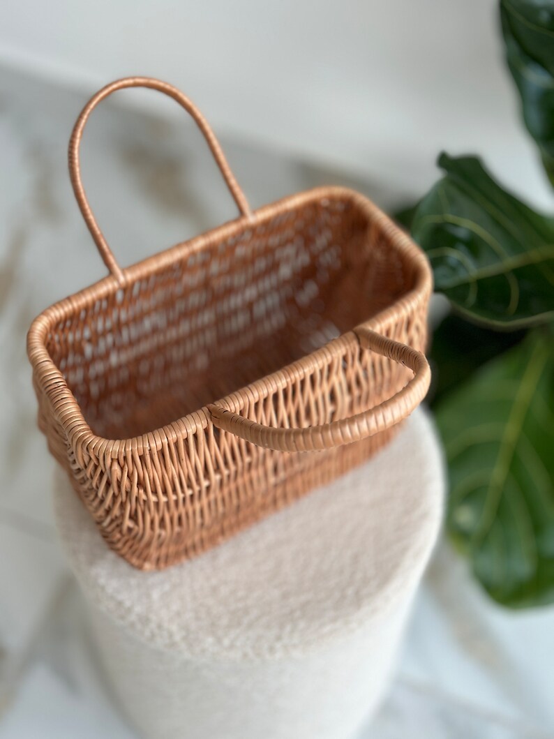 May include: A woven wicker basket with a single handle. The basket is light brown and has a rectangular shape.