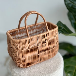 May include: A woven wicker basket with a rectangular shape and a single handle. The basket is light brown and has a natural, rustic look.
